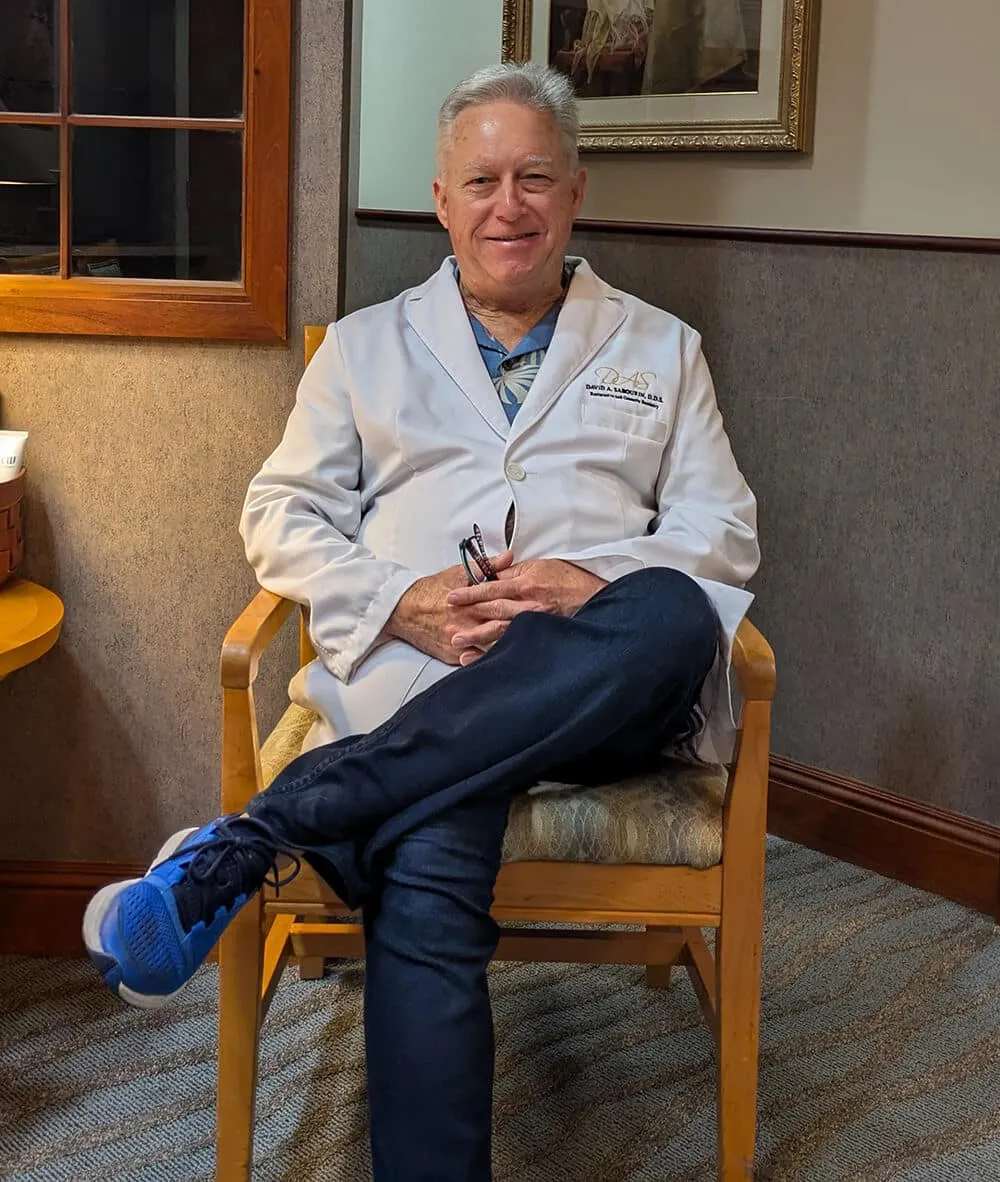 Dr. David A. Sabourin, smiling, seated in his wood-paneled office in a white coat
